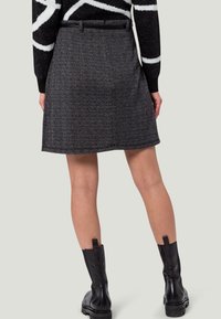 Musta ja harmaa tweed-hame suoralla leikkauksella, jossa on vyötärö ja hienovarainen rakenne. Yhdistetty mustiin nahkasaappaisiin, jotka ulottuvat nilkkoihin.