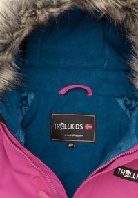Rozā ziemas jakas iekšpuse ar zilu flīsa oderi, pelēku mākslīgo kažokādu apdari, un etiķeti, kurā ir uzraksts "TROLLKIDS" un tā interneta vietnes dati.