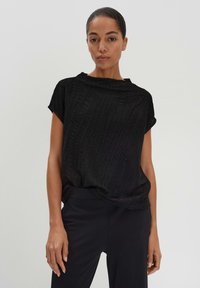 T-shirt noir texturé avec une coupe ample, des manches courtes et un col rond. Porté avec un pantalon noir.