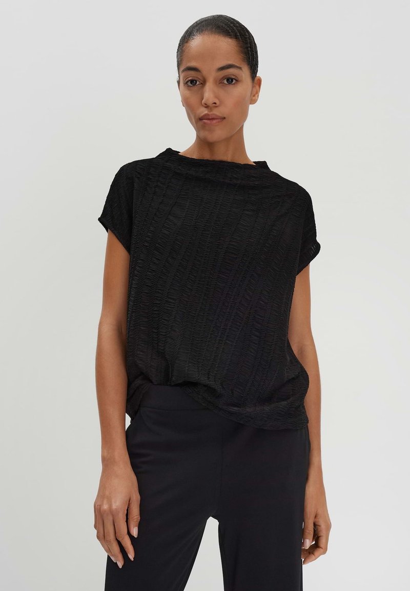 T-shirt noir texturé avec une coupe ample, des manches courtes et un col rond. Porté avec un pantalon noir.