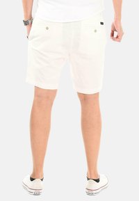 Weiße Baumwollshorts mit einem lässigen Schnitt, ausgestattet mit zwei Gesäßtaschen mit Knopfverschlüssen und kombiniert mit weißen Sneakers.