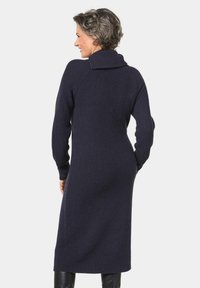 Navy-blaues geripptes Strickkleid mit hohem Kragen, langen Ärmeln und taillierter Silhouette, die bis zur Mitte der Wade reicht. Das strukturierte Material verleiht Tiefe.