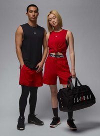 Sort ærmeløs top, røde shorts og sorte leggings på en mandlig model. Kvindelig model i en knyttet rød top og røde shorts holder en sort taske.