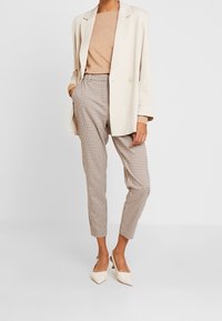Beige Blazer, brauner Pullover und karierte Hose in Brauntönen; spitze nudefarbene High Heels; glattes Gewebe mit taillierter Passform.