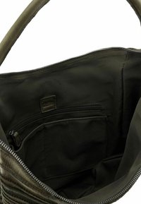 Interno di una borsa a tracolla di tessuto verde oliva con chiusura a zip, dotata di una tasca con zip e una tasca piatta, texture liscia e design foderato.