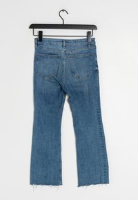 Jeans a zampa d'elefante in denim blu chiaro, con orlo grezzo, due tasche posteriori e vita standard, esposti su una gruccia nera.