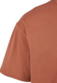 Tričko s krátkým rukávem v měděné barvě, vyrobené z měkké bavlny, s kulatým výstřihem a hladkou texturou, se jemným švem podél lemu.
