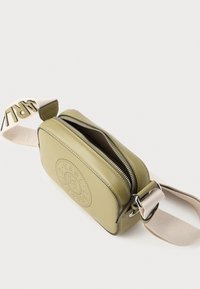 Prostokątny oliwkowozielony worek wykonany z gładkiej skóry, z zamkiem błyskawicznym oraz kremowym regulowanym paskiem z detalem logo.