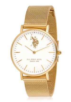 Montre en maille dorée avec un cadran blanc, des index horaires dorés et un logo représentant un joueur de polo. Boîtier rond lisse avec des marquages des minutes.