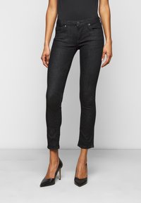 Zwarte skinny jeans van denimstof met een taillehoogte halverwege, voorzien van vijf zakken en subtiele vervaging, gecombineerd met zwarte schoenen met hoge hakken.