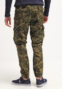 Kamouflage cargobyxor i gröna nyanser, med flera fickor, elastiska muddar och en avslappnad passform. Bärs med mörka sneakers.