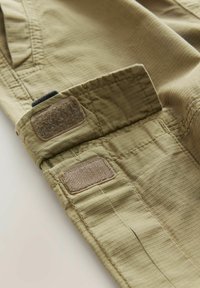 Poignet en tissu khaki avec des patchs en velcro, présentant un motif texturé et côtelé. Convient pour un usage décontracté ou en extérieur.