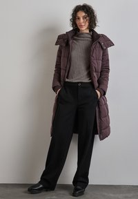 Langer burgunderfarbener Daunenmantel mit hohem Kragen, grauer gerippter Rollkragensweater und schwarzen weit geschnittenen Hosen. Schwarze Lederschuhe. Einfaches Design.