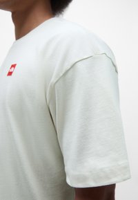 Short-sleeve mint green t-shirt made of soft cotton; features a small red logo on the chest and a relaxed fit with stitched hems.
