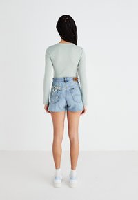 Shorts en denim bleu clair avec un ourlet effiloché, ornés de motifs floraux sur les poches arrière, associés à un haut à manches longues vert clair.