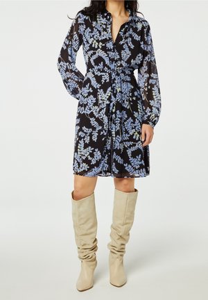 Robe chemise noire à motifs floraux avec des manches longues et transparentes, une taille à nouer et des bottes slouch beiges jusqu'aux genoux. Texture de tissu lisse.