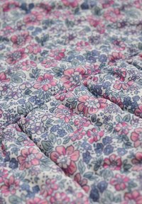 Tissu floral avec une base blanche ornée de motifs floraux complexes en rose, bleu et vert. Doux, texturé avec des plis froncés.