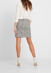 Grijs geruite mini-jurk met een strakke pasvorm, voorzien van een subtiel riemdetail. Gepaarde met crèmekleurige enkellaarsjes en een witte blouse.