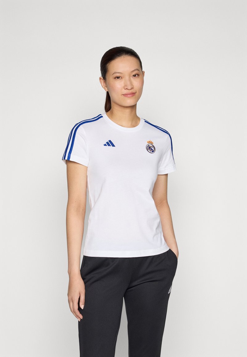 Bílý sportovní tričko s modrými pruhy na rukávech, s kulatým logem Real Madrid a značkou Adidas. Měkká tkanina, standardní střih.