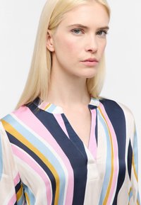 Multifarvet bluse med lodrette striber i pink, blå, marineblå og gul, med V-udskæring og blødt, glat stof.