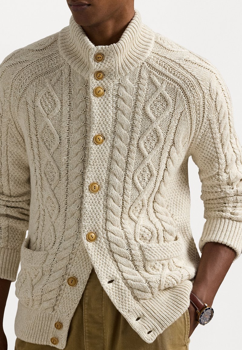 Cardigan lavorato a maglia color crema con un alto colletto, grandi bottoni in legno, intricati motivi a treccia e due tasche frontali.