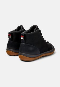 Zapatillas negras de media caña hechas de tela texturizada con suela de goma. Presentan un logo rojo y un acento suave en el talón negro.