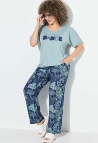 Lichtblauwe T-shirt met "DANCE" in textuurdetail in marineblauwe letters, gecombineerd met gestreepte marineblauwe en teal broek met paisleypatronen. Witte instapsandalen.