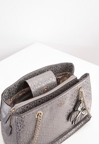 Gestructuurde handtas van metallic zilveren materiaal, met een monogrampatroon, ritssluiting compartimenten en een decoratieve vlinderaccent.