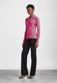 Pielāgots rozā kardigāns ar apkakles dekoltē un pogu aizdari, kombinēts ar melniem platām biksēm un melniem sandaliem ar siksniņām.