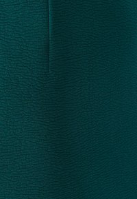 Grönt texturerat tyg med ett vågmönster, som har en slät yta och subtil glans. Passar för kläder eller accessoarer.