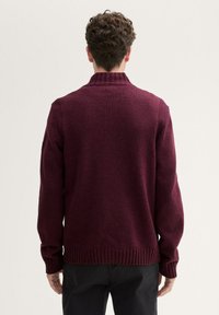 Bordeauxfarbener Wollpullover mit geripptem Kragen und Bündchen, gestrickter Textur und lockerer Passform, mit Details an den Schulternähten.