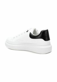Zapatilla blanca con parte superior de cuero liso, acento de talón sintético negro, diseño de punta redonda y una suela blanca gruesa con agarre texturizado.
