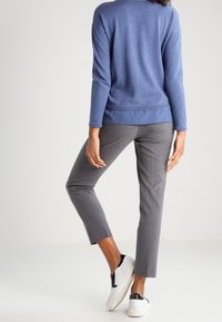 Blue sweater with long sleeves and a rounded hem paired with gray tapered trousers and white sneakers featuring black accents.