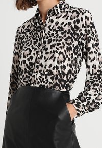 Leopard print blouse in lightweight fabric with a classic collar, long sleeves, and a button front, paired with a high-waisted leather skirt.