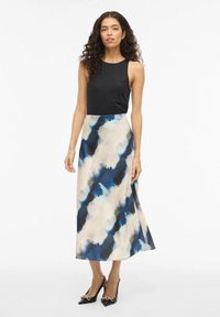 Sort ermeløs topp kombinert med et flytende, flerfarget midiskjørt med abstrakte mønstre i blått og krem. Høye hæler fullfører antrekket.