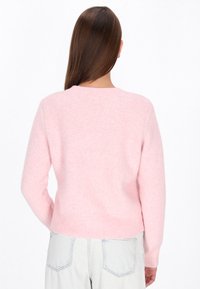 Helles rosa, kuscheliges Sweatshirt mit rundem Ausschnitt und langen Ärmeln. Rippenbündchen an Saum und Ärmeln. Die Rückansicht zeigt die weiche Textur und die lockere Passform.