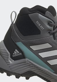 Graue und schwarze wasserdichte High-Top-Schuhe aus strukturiertem Material mit Mesh-Akzenten und einem türkisfarbenen Streifen. Sie verfügen über eine robuste Au ßensohle für besseren Halt.