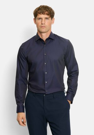 Navy blue long-sleeve shirt with a buttoned collar, front buttons, and a smooth texture, paired with dark trousers.