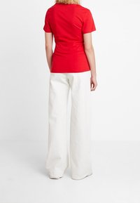 Camiseta roja de manga corta combinada con pantalones blancos holgados, que presentan un diseño de color sólido y una textura suave de algodón.