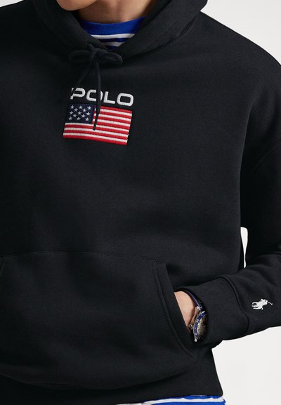 Svart hettegenser i fleece med frontlomme, snor i hetten og brodert amerikansk flagg-logo. Hvit polo-logo på ermet.