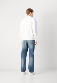 Felpa bianca con polsini e orlo a coste, abbinata a jeans azzurri chiari con un effetto sbiadito e taglio dritto. Sneakers bianche completano il look.