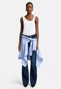 Witte tanktop, lichtblauw shirt om de taille geknoopt, donkerblauwe flared jeans, zwarte riem met ronde zilveren gesp, spitse zwarte hakken.