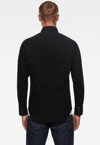 Czarna koszula z kordurojowej tkaniny z długimi rękawami, mankietami na guziki i tylnym karczkiem. Posiada subtelną teksturę i zakrzywiony krój hem.