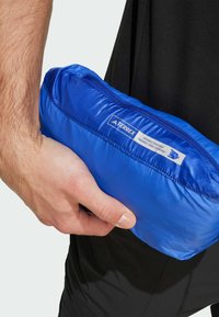 Blauwe geïsoleerde tas met een ritsluiting, voorzien van een textuurafwerking en een merklabel, vastgehouden in een hand naast zwarte kleding.