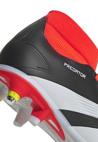 Scarpa da calcio nera con collare a calza rosso, tomaia texturizzata, suola intermedia bianca e suola esterna rossa con tacchetti gialli. Marchio visibile sul lato.