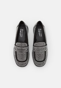 Des chaussures noires à enfiler au design plat, ornées d'embellissements en argent. Elles présentent un bout arrondi et une bande étroite sur le devant.
