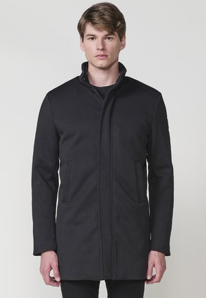 Abrigo exterior negro con cuello alto, cierre de cremallera y dos bolsillos frontales. Fabricado en un tejido suave con un corte ajustado.