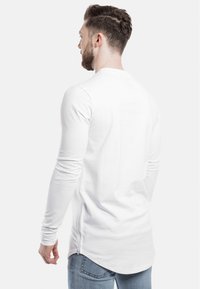 Weißes Langarmshirt mit rundem Halsausschnitt, mit abgerundetem Saum und seitlichen Reißverschlussdetails. Süßes, baumwollähnliches Material.