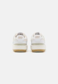 White Nike sneakers with a smooth leather upper, cream accents, a textured rubber sole, and subtle branding on the heel.