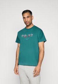 T-shirt de algodão em verde-água com decote redondo, mangas curtas e uma impressão gráfica com desenhos circulares na frente.